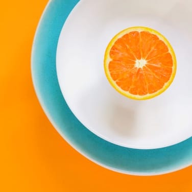 an orange cut in half over light blue and a white plate on an orange table.