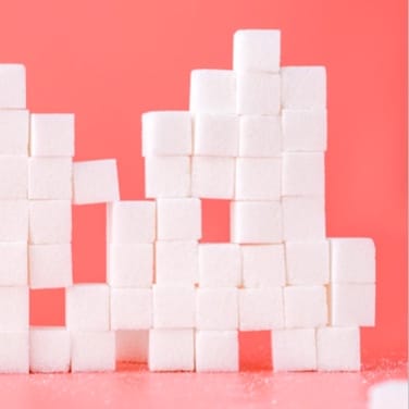 Sugar cubes pile on top of each other on a pink room.